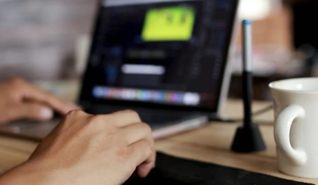 a person's hands typing on a laptop keyboard, with a cup of coffee and a lamp in the background on a wooden desk